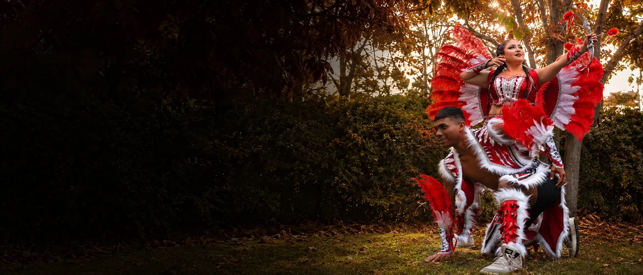 Pareja de bailarines con el traje de Tobas rojo completo: ella con penacho y arco, él con chaqueta, faldón y puñeras